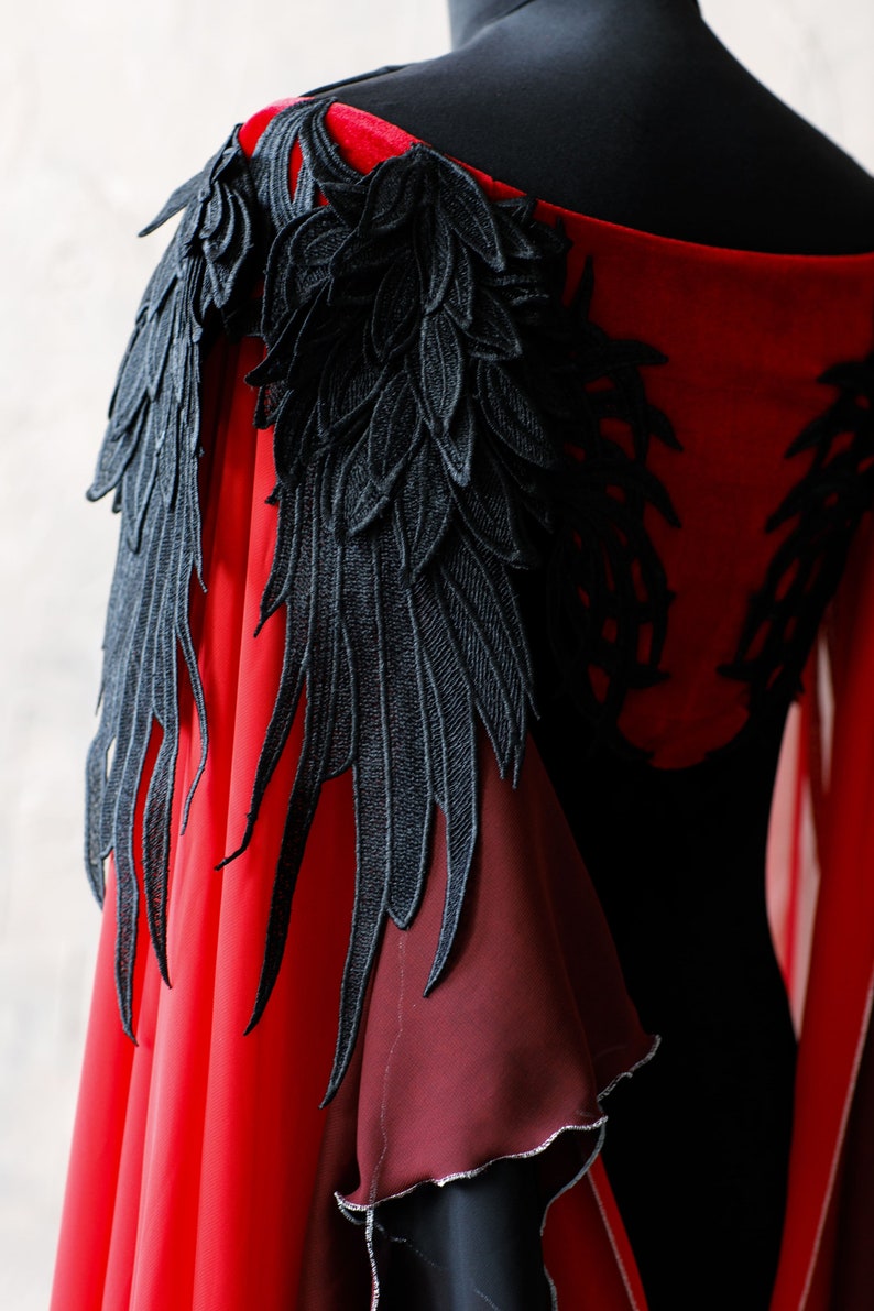 May include: A red and burgundy velvet cape with black lace wings. The wings are detailed with intricate feather designs.