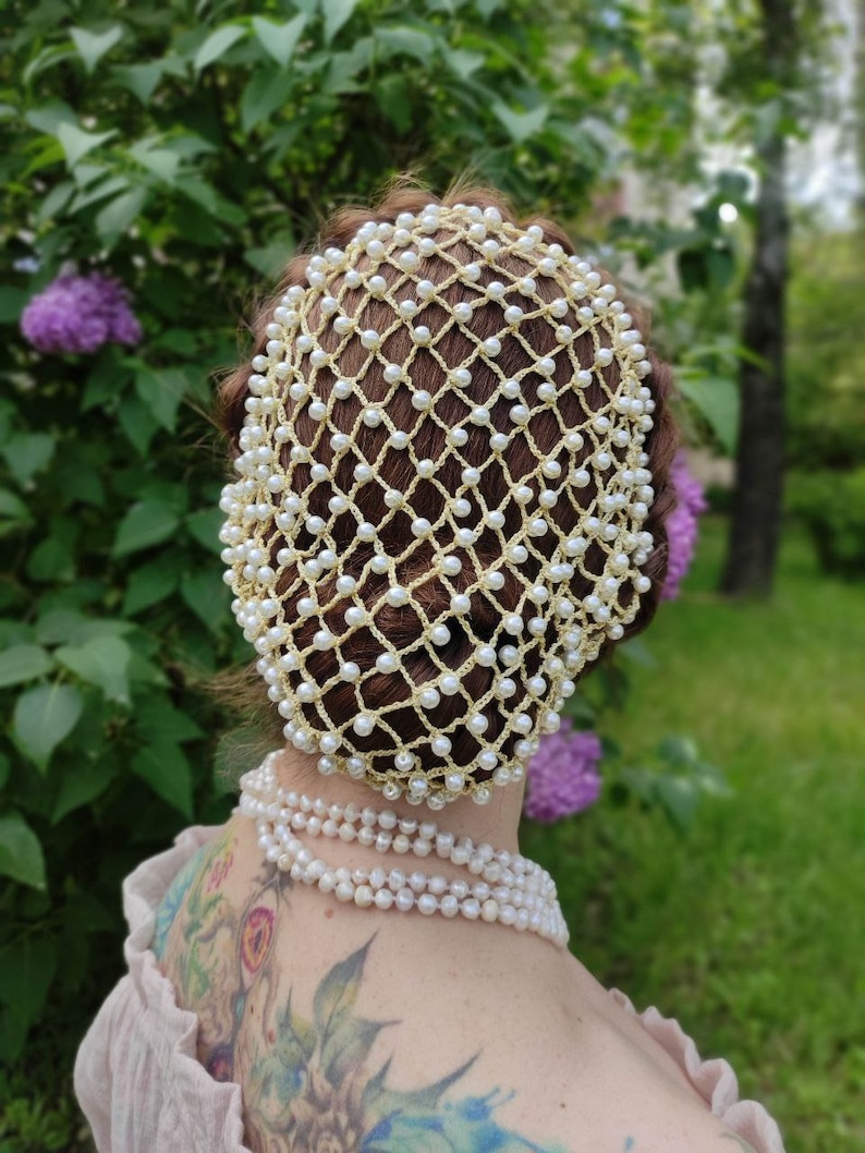 May include: A white pearl hair net with a gold crochet design. The net is worn on a person's head and covers the hair.