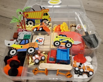 May include: A clear plastic storage container filled with various toy construction vehicles, including a yellow dump truck, a red truck, a yellow excavator, and a black shovel. The container also includes small wooden blocks, a red and white traffic cone, and a small pile of white rocks.