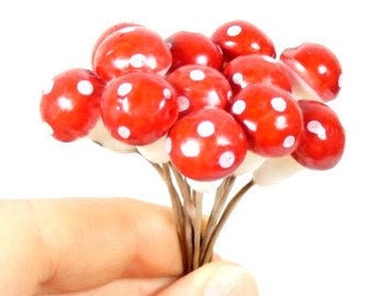 Può includere: Un mazzo di funghi decorativi rossi e bianchi con pois bianchi. I funghi sono su steli sottili di filo metallico.