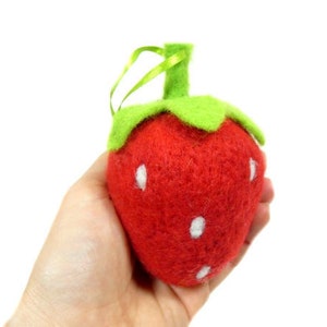 Może przedstawiać: Ozdoba w kształcie truskawki z filcu z zielonym filcowym szypułką i liśćmi. Truskawka jest czerwona z białymi kropkami z filcu.