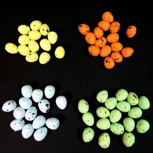 May include: Four groups of speckled Easter eggs in different colours: yellow, orange, light blue, and green. The eggs are arranged in a square pattern on a black background.