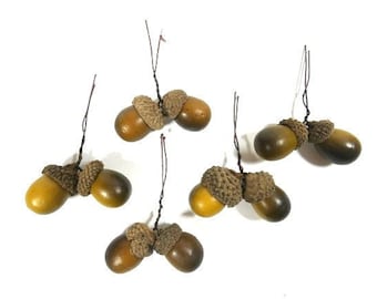 May include: Six brown and tan acorns with wire stems. The acorns are arranged in pairs.