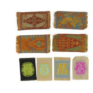 May include: A selection of miniature woven rugs and embroidered sachets. The rugs display detailed patterns in red, orange, and blue hues. The sachets are embroidered with letters and symbols in various colours, including green, blue, and pink.