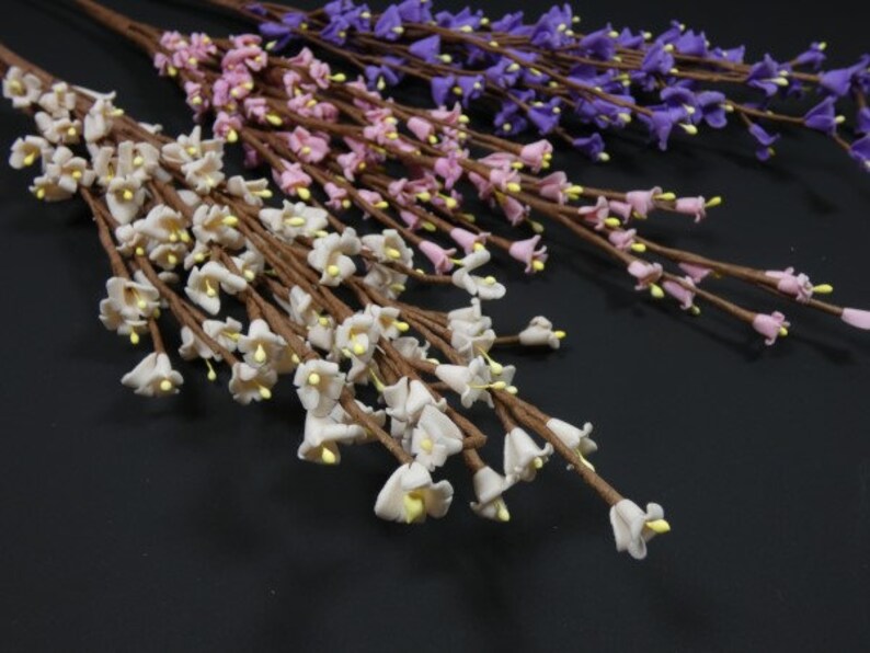 May include: Three bunches of artificial flowers with small bell-shaped blossoms. The flowers are white, pink, and purple.