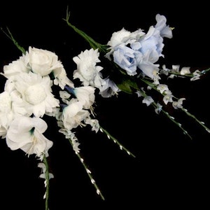 May include: Two bouquets of artificial flowers. One bouquet is white with a mix of roses and carnations. The other bouquet is light blue with a mix of roses and carnations.