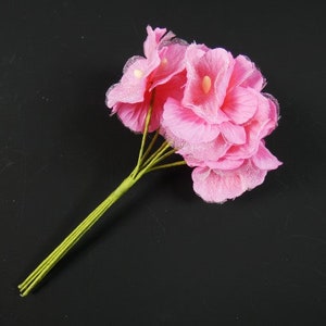 May include: A bouquet of pink silk flowers with green stems. The flowers are arranged in a cluster and have a delicate, ruffled texture.
