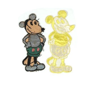 May include: Two vintage-style Mickey Mouse patches. One patch is fully colored with a tan face, gray body, green shorts, and black shoes. The other is a yellow outline of Mickey Mouse.