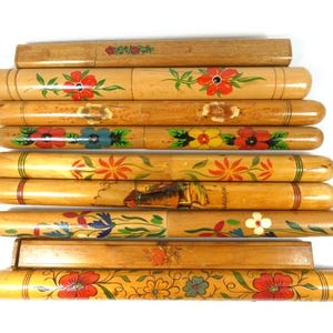 Puede incluir: Un juego de diez estuches de lápices de madera con diseños florales pintados a mano en tonos rojos, amarillos, azules y verdes.