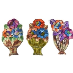 May include: Three embroidered fabric appliques featuring floral arrangements in vases. The appliques are in shades of orange, pink, blue, green, and brown.