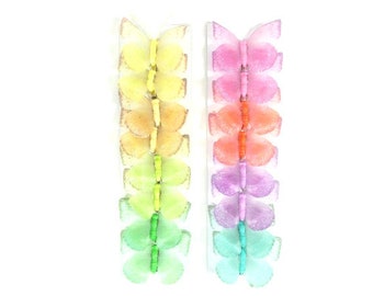 May include: A set of 18 decorative butterfly wall decals in a rainbow gradient of colors. The butterflies are arranged in two rows, with each row containing nine butterflies. The butterflies are made of a translucent material and have a delicate, iridescent finish.