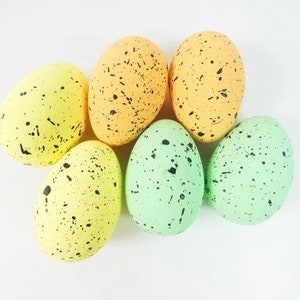 May include: Six speckled Easter eggs in various shades of green, yellow, and orange. The eggs are arranged in a semi-circle on a white background.