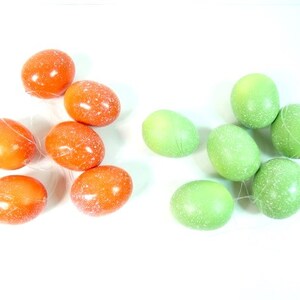 May include: A group of orange and green speckled Easter eggs, tied together with string. The eggs are arranged in a cluster, with the orange eggs on the left and the green eggs on the right.