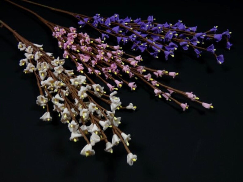 May include: Three sprigs of artificial flowers with small bell-shaped blooms. The flowers are white, pink, and purple.