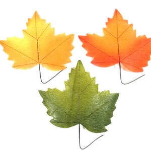 Könnte beinhalten: Drei künstliche Ahornblätter in Herbstfarben: Gelb, Orange und Grün. Jedes Blatt hat ein detailliertes Adernmuster und einen Drahtstiel zur einfachen Platzierung. Ideal für herbstliche Bastelarbeiten und Dekorationen.