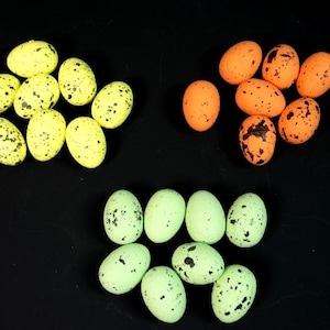 May include: Assortment of speckled Easter eggs in yellow, green and orange colours. The eggs are arranged in three groups on a black background.