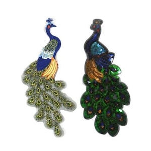 Könnte beinhalten: Zwei Pfauen-Stickerei-Patches, einer mit blauen und goldenen Akzenten und einem grünen Schwanz, der andere mit grünen und goldenen Akzenten und einem blauen Schwanz.