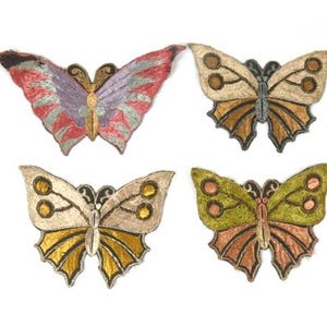 Puede incluir: Cuatro parches de mariposa bordados en diferentes colores. Las mariposas son en tonos de rosa, morado, beige, dorado, verde y marrón.