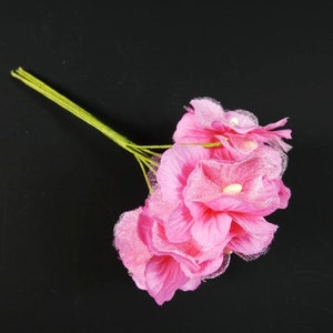 May include: A bouquet of pink artificial flowers with green stems. The flowers have a delicate, layered texture.