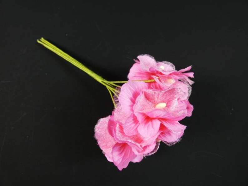 May include: A bouquet of pink artificial flowers with green stems. The flowers have a delicate, layered texture.
