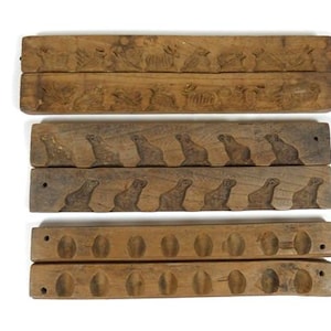 May include: A collection of six antique wooden molds. Two molds feature animal designs, two have a series of seal carvings, and the final two have circular indentations. The molds are made of aged, brown wood.