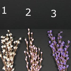 May include: Three bunches of artificial flowers, each with a different color. The first bunch is white, the second is pink, and the third is purple. The flowers are all small and delicate, and they are arranged in a simple, elegant way.
