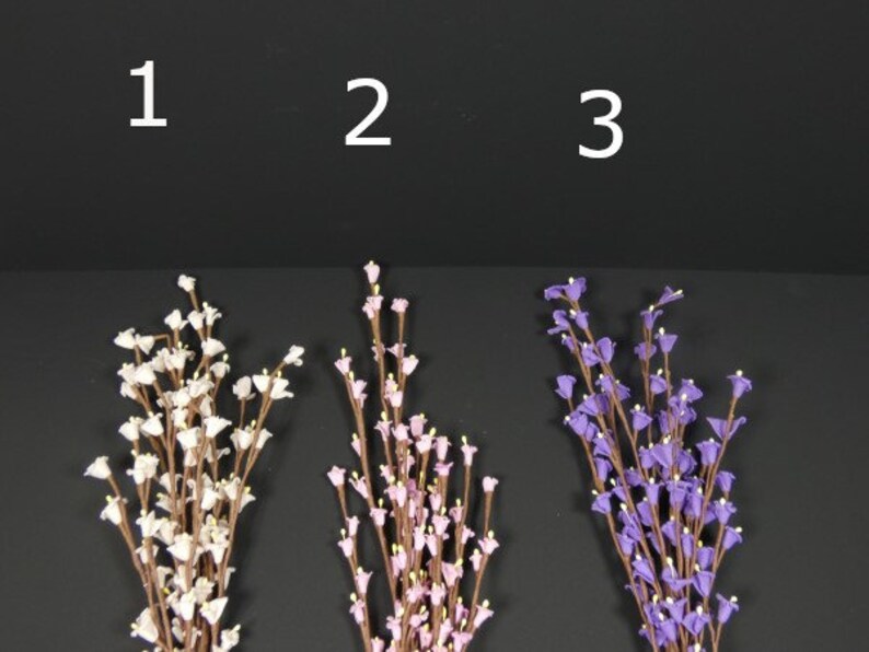 May include: Three bunches of artificial flowers, each with a different color. The first bunch is white, the second is pink, and the third is purple. The flowers are all small and delicate, and they are arranged in a simple, elegant way.
