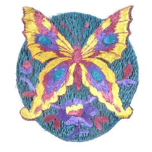 Puede incluir: Un parche bordado de mariposa colorido con acentos amarillos, morados, rojos y azules sobre un fondo azul verdoso.