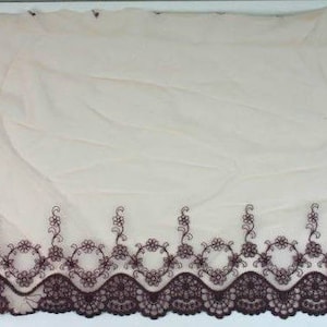 May include: A close-up of a beige sheer fabric with a brown embroidered lace trim. The lace features a scalloped edge and a delicate floral design.