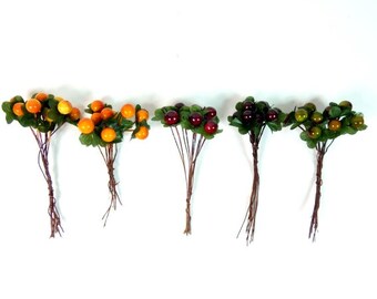 May include: Six bunches of artificial berries with green leaves. The berries are in various colors, including orange, red, and green.