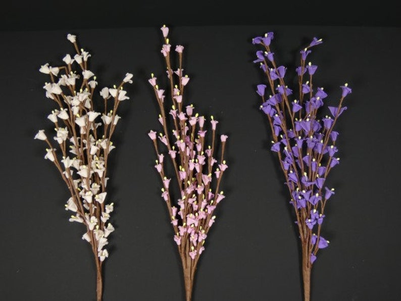 May include: Three bunches of artificial flowers with small bell-shaped blooms. The flowers are white, pink, and purple.