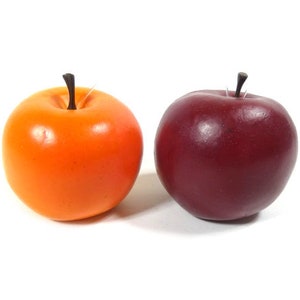 Op de afbeelding: Twee kunstmatige appels, een oranje en een rode, op een witte achtergrond.