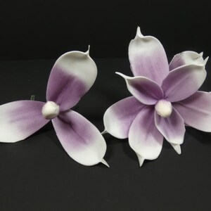 May include: Two artificial magnolia flowers with white petals and purple centers. The flowers are made of a soft, fabric-like material.