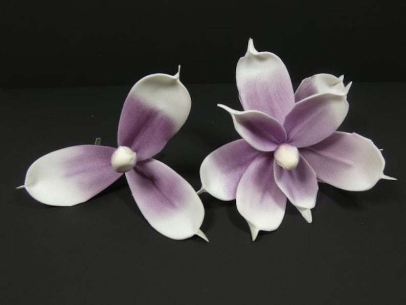 May include: Two artificial magnolia flowers with white petals and purple centers. The flowers are made of a soft, fabric-like material.