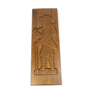 Pu&ograve; includere: Un tagliapasta in legno a forma di persona che tiene un bastone. Il tagliapasta &egrave; intagliato con dettagli intricati e ha una finitura marrone.