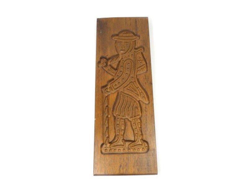Pu&ograve; includere: Un tagliapasta in legno a forma di persona che tiene un bastone. Il tagliapasta &egrave; intagliato con dettagli intricati e ha una finitura marrone.