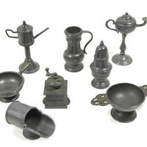 Może przedstawiać: Kolekcja ośmiu miniaturowych przedmiotów kuchennych z cyny, w tym dzbanek do śmietanki, pieprzniczka, młynek do kawy, lampa, miska i dwie tace do serwowania.