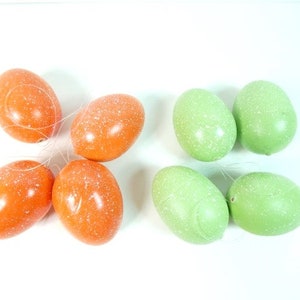 May include: Six speckled Easter eggs, four orange and two green, are strung together with clear thread.