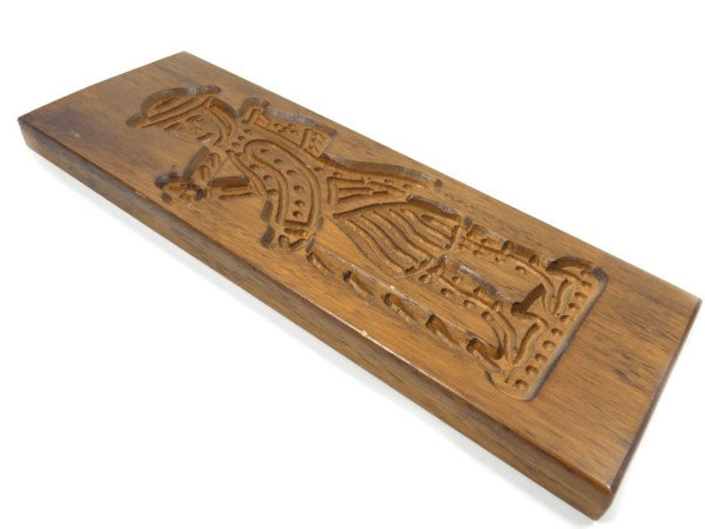 Pu&ograve; includere: Uno stampo per biscotti in legno con una scultura dettagliata di una persona in costume tradizionale. Lo stampo &egrave; in legno marrone scuro e ha una finitura liscia e lucida.