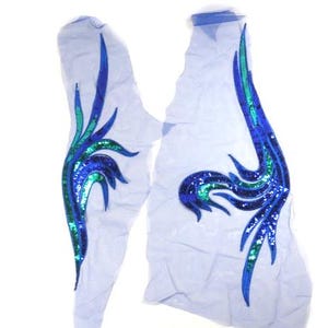 May include: Two blue and green sequined fabric appliques in the shape of a stylized bird wing. The appliques are on a sheer white fabric background.