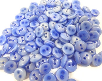 May include: A large pile of light blue plastic buttons with two holes each. The buttons are smooth and shiny.
