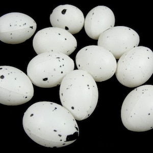 May include: A collection of white speckled eggs with black spots. The eggs are arranged in a circle on a black background.