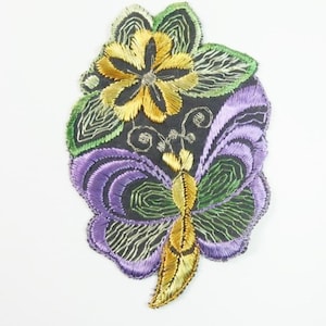 Puede incluir: Parche bordado para planchar con una mariposa morada y verde con detalles dorados y una flor amarilla con hojas verdes.