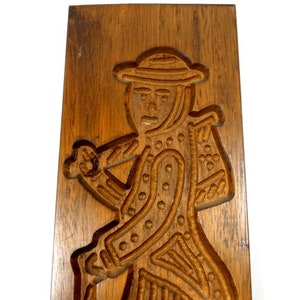 Pu&ograve; includere: Uno stampo per biscotti in legno con una scultura dettagliata di una persona che indossa un cappello e porta un bastone. Lo stampo &egrave; in legno marrone scuro e ha una superficie liscia e lucida.