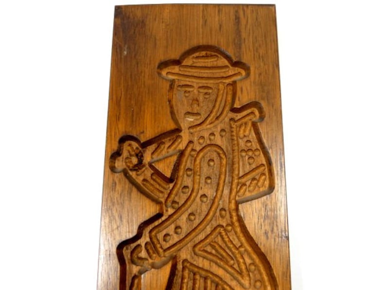 Pu&ograve; includere: Uno stampo per biscotti in legno con una scultura dettagliata di una persona che indossa un cappello e porta un bastone. Lo stampo &egrave; in legno marrone scuro e ha una superficie liscia e lucida.
