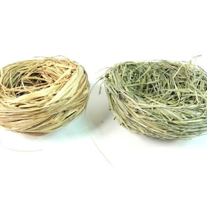 May include: Two woven bird nests, one made of natural straw and the other made of green grass.