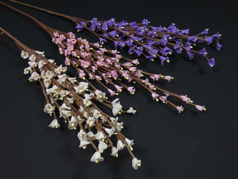 May include: Three artificial flower stems with small bell-shaped flowers. The stems are brown and the flowers are white, pink, and purple.
