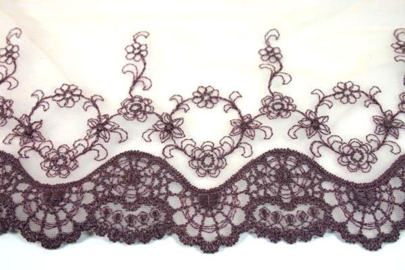 May include: A close-up of a brown lace trim with a scalloped edge. The lace has a delicate floral pattern and is perfect for adding a touch of elegance to any project.