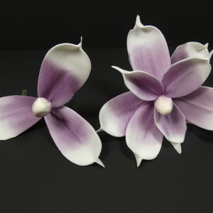May include: Two artificial magnolia flowers with white petals and purple centers. The flowers are made of a soft, fabric-like material.