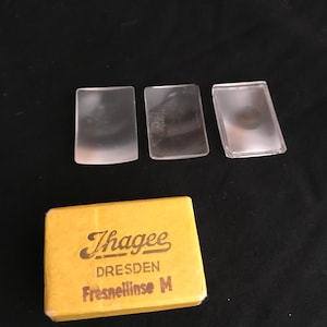 May include: Three clear plastic Fresnel lenses in a yellow box with the text "Thagee Dresden Fresnellinse M".
